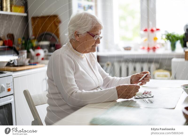 Senior woman taking pills in her home kitchen people senior mature female elderly house old aging domestic life grandmother pensioner retired retirement