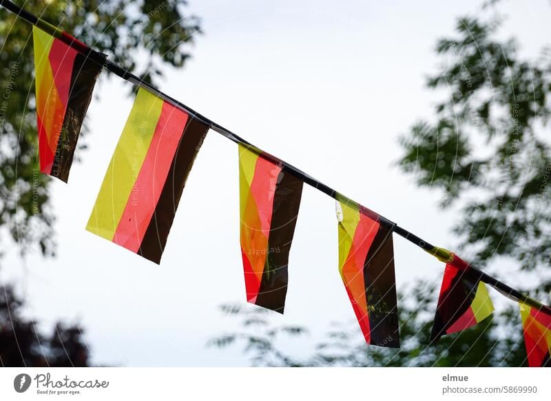 Garland with small square black, red and gold flags between trees Paper chain celebrations Foot ball Public viewing pennant chain Feasts & Celebrations