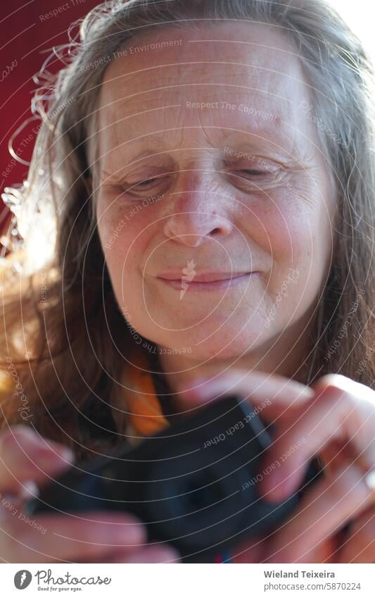 Smiling senior woman with loose hair looks at the back screen of a digital camera. She enjoys the photo she sees natural aged closeup beauty looking female