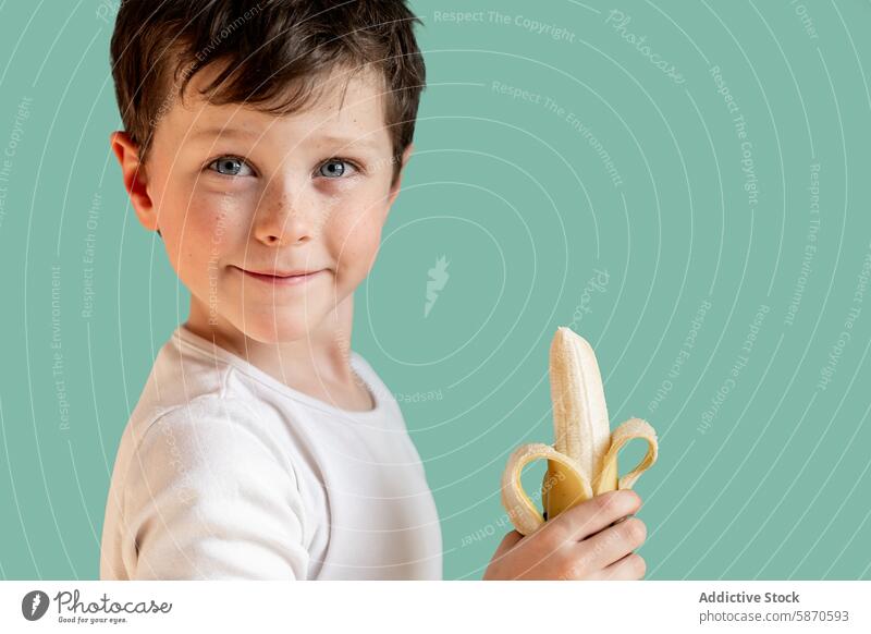 Young boy holding a banana and smiling in a studio child kid fruit snack healthy smile happy nutrition food young male portrait looking away eating white shirt