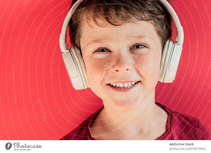 Smiling boy with headphones against a red background smile studio kid youth happy joy music technology gadget device listening enjoyment cheerful portrait