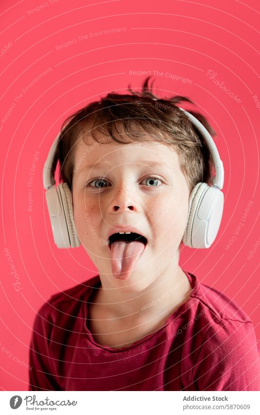 Playful young boy with headphones sticks out tongue child kid studio playful looking at camera red background male make face red shirt wireless gadget device