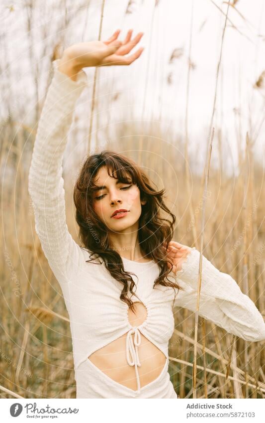 Young woman enjoying solitude in a natural setting nature peaceful curly hair reeds stylish outdoor serene graceful white top knotted top dry reeds enjoyment