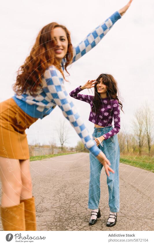 Two joyful friends playing and posing on a country road woman smile casual fashion dance interaction expression happiness countryside rural outdoor day fun pose