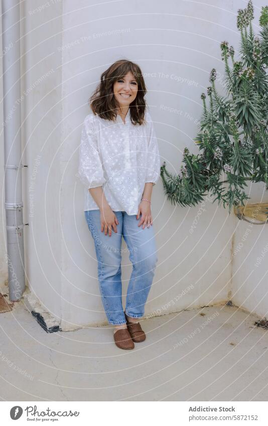 Casual woman smiling standing outdoors smile casual fashion plant wall happiness joyful adult female blouse jeans textured serene tranquil stylish modern