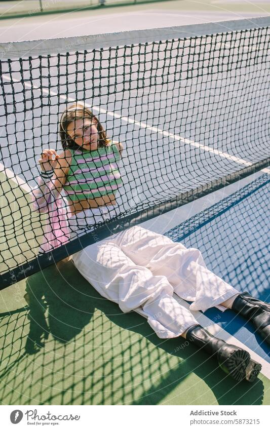 Stylish Woman Relaxing Against Tennis Net in Trendy Outfit woman tennis court relax sunny leisure lifestyle striped tank top net enjoyment day casual outdoor