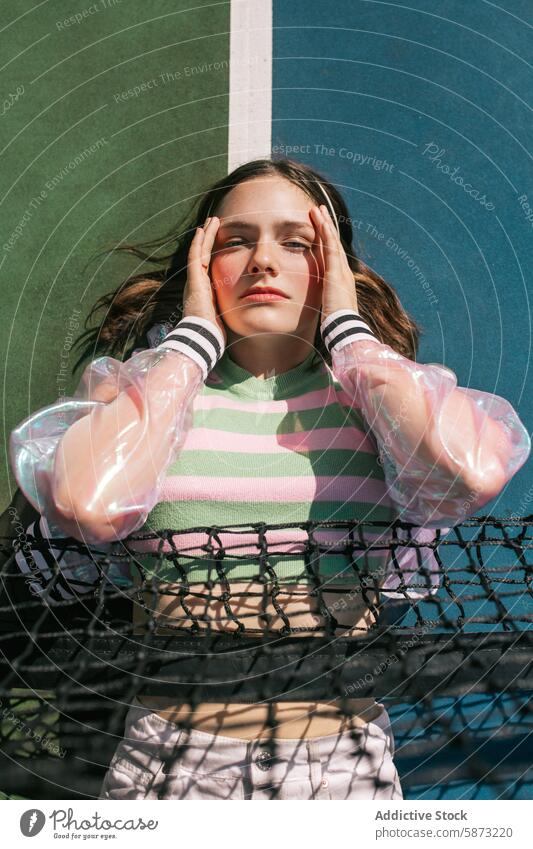 Young woman relaxing on a tennis court young colorful attire serene expression peaceful atmosphere unwinding hands face bright light outdoor leisure recreation