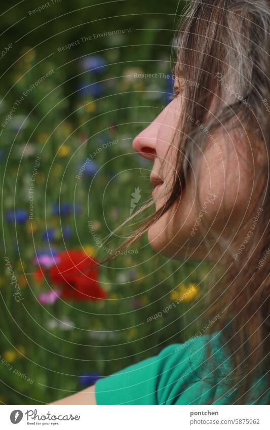 a woman in profile in front of a meadow of flowers Flower meadow wild flowers variegated blurred hazy Red purple poppies Nature Summer Meadow flower Green Woman