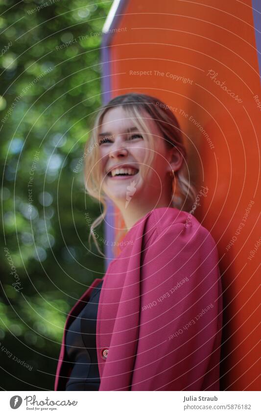 Young pretty woman in a pink blazer stands in front of an orange wall Young woman Long-haired cheerful Application photo portrait Laughter Curl well dressed