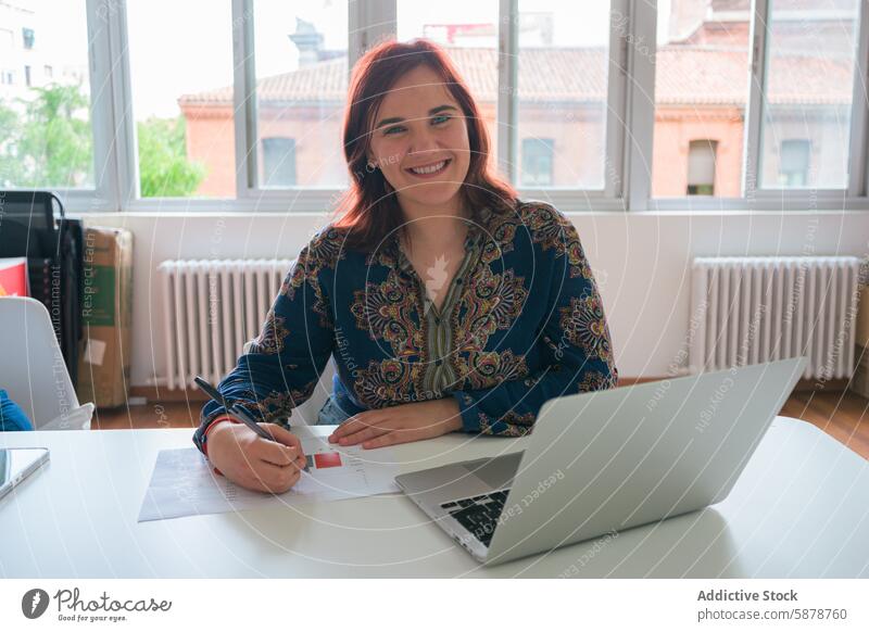 Smiling businesswoman working at desk with laptop office smiling professional workplace document cheerful employee manager technology internet computer paper