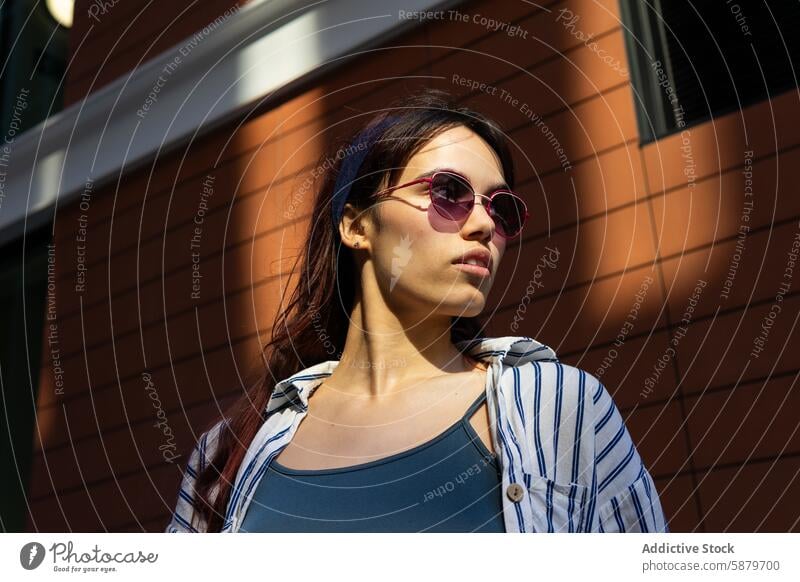 Casual woman in sunglasses leaning against a brick wall spring sunlight urban casual style fashion young trendy outdoor city leisure relaxed portrait female