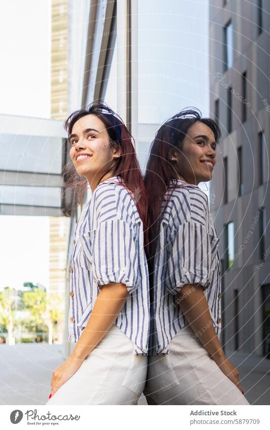 Cheerful woman reflecting on urban building glass reflection cheerful spring portrait cityscape striped shirt casual building façade outdoors daytime vibrant