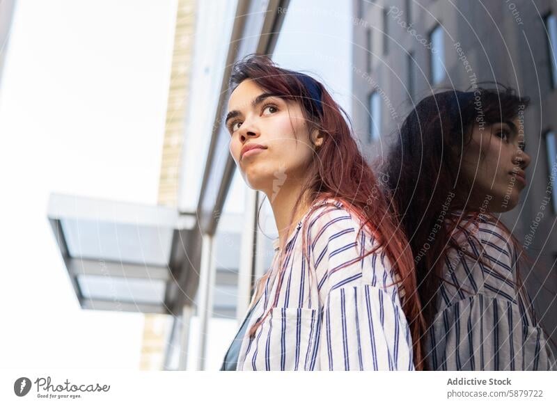 Young woman gazing upwards in urban setting young reflective thoughtful gaze building glass city portrait spring outward introspective energy flowing hair