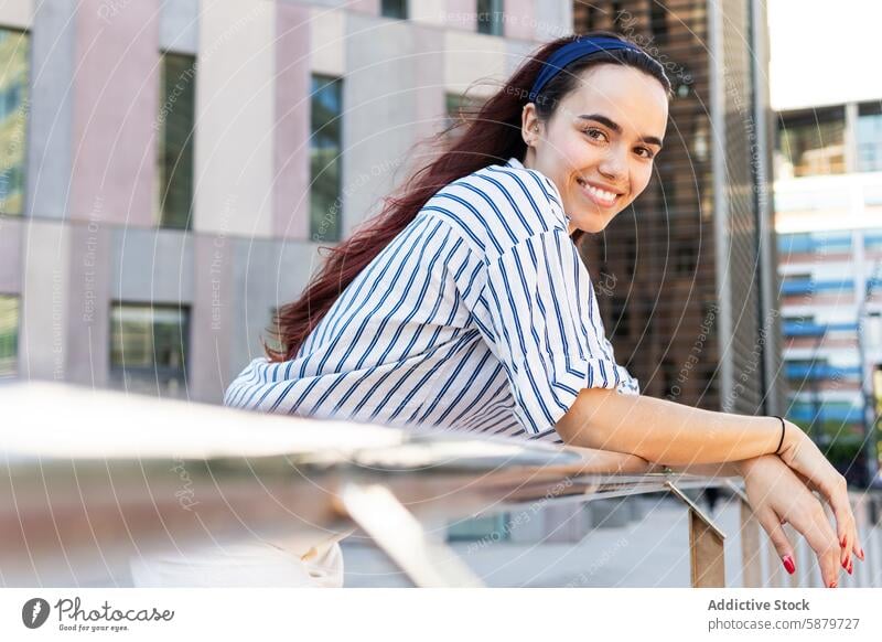 Young woman in striped blouse smiling in urban setting spring portrait smile cheerful railing building sunny day young female red hair blue environment outdoor