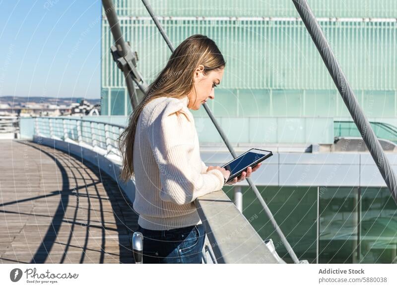 Woman using tablet on a sunny bridge woman cityscape technology sky modern footbridge device gadget outdoor looking down female sunlight day urban