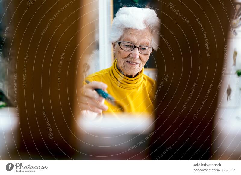 Elderly woman in yellow engaged in painting elderly senior mature artist creative hobby leisure activity concentration focused indoor glasses white hair