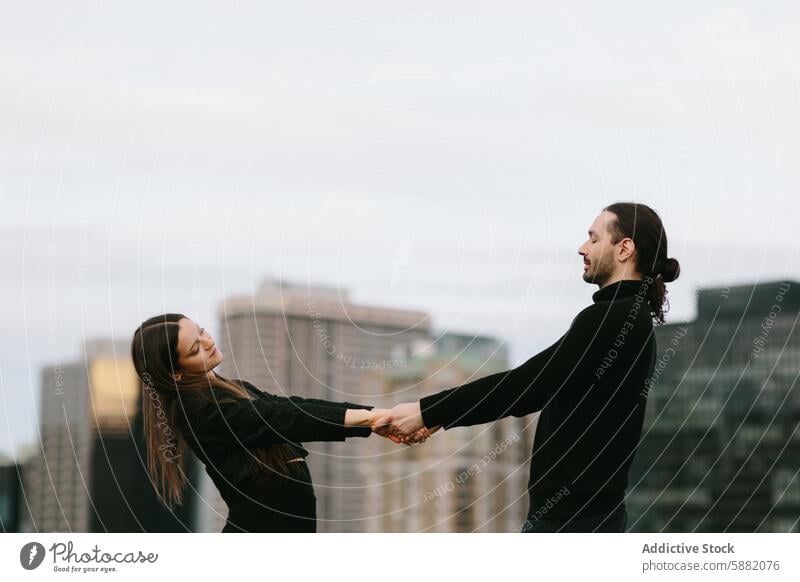 Couple holding hands and dancing on a rooftop couple cityscape urban man woman dance bonding love eyes closed relationship skyline high-rise buildings outdoors