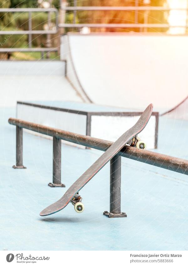 Skateboard leaning against a rail in a skatepark. skateboard ramp empty outdoor sports recreation skating sunny deck wheels grind trick balance urban extreme