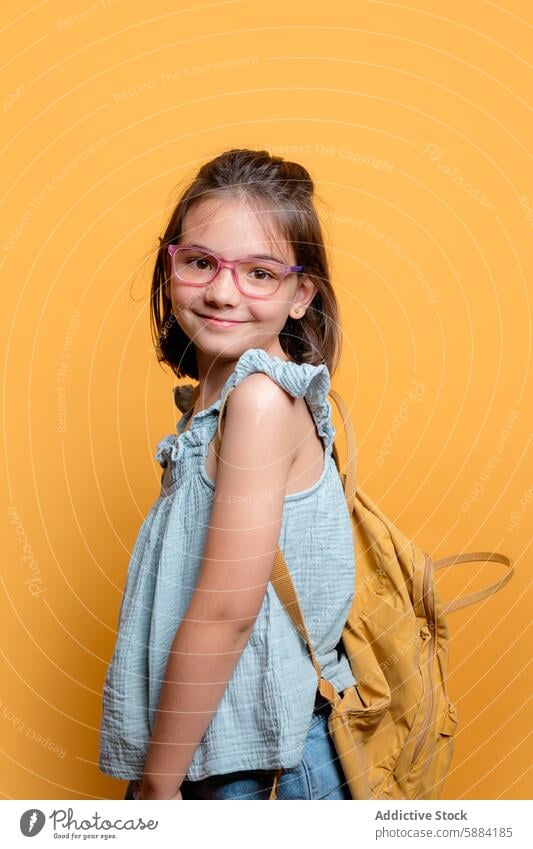 Young schoolgirl with backpack smiling on yellow background smile glasses backdrop child student studio portrait happy cheerful fashion accessory ruffled top