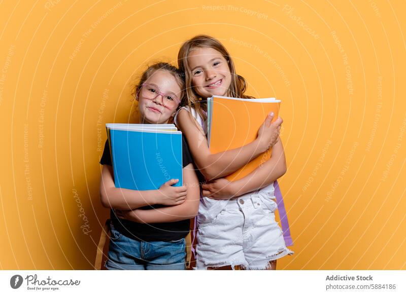 Two smiling girls holding books against a yellow background smile education school studio happy childhood friendship embrace joy learning casual student