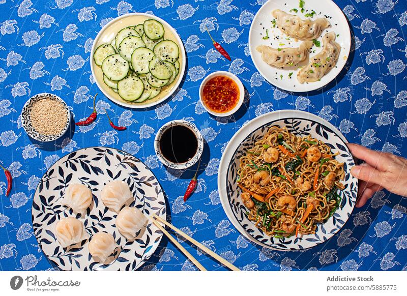 Top view of Chinese dumplings, noodles, and cucumber salad chinese food person top view sesame shrimp tableware floral tablecloth soy sauce chili sauce