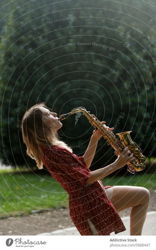 Woman playing saxophone in a park with eyes closed woman music passion outdoor instrument feel green dress pattern red lush leaf nature summer relax performance