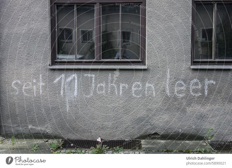 gray house wall with slogan in white writing : empty for 11 years Graffiti housing crisis housing shortage Facade Real estate market House hunting dwell Rent