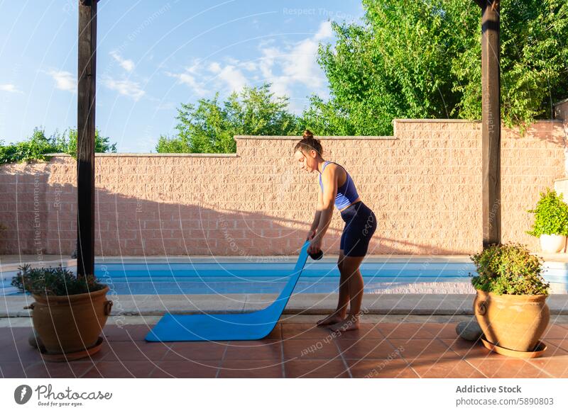 Woman preparing for poolside yoga session woman outdoor fitness exercise health wellness tranquil sunny backyard mat unrolling attire active lifestyle calm