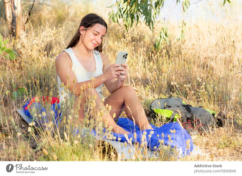 Young woman relaxing and using smartphone while hiking young break grass seated backpack shade trend lifestyle nature outdoor relaxation leisure sunny summer