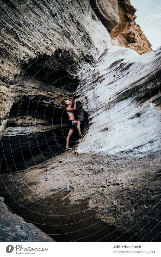 Young man climbing a rock near a cave on a sunny day adventure summer holiday nature outdoor exploration travel daring muscular swim trunk daytime natural