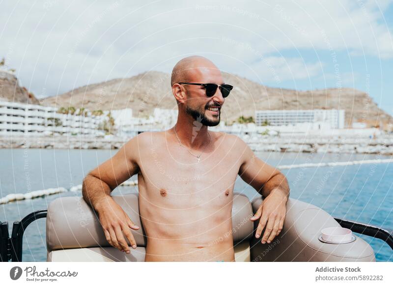 Bald man enjoying summer on a boat with scenic backdrop holiday bald sunglasses smile coastline mountain ocean relaxation vacation beach travel leisure cheerful