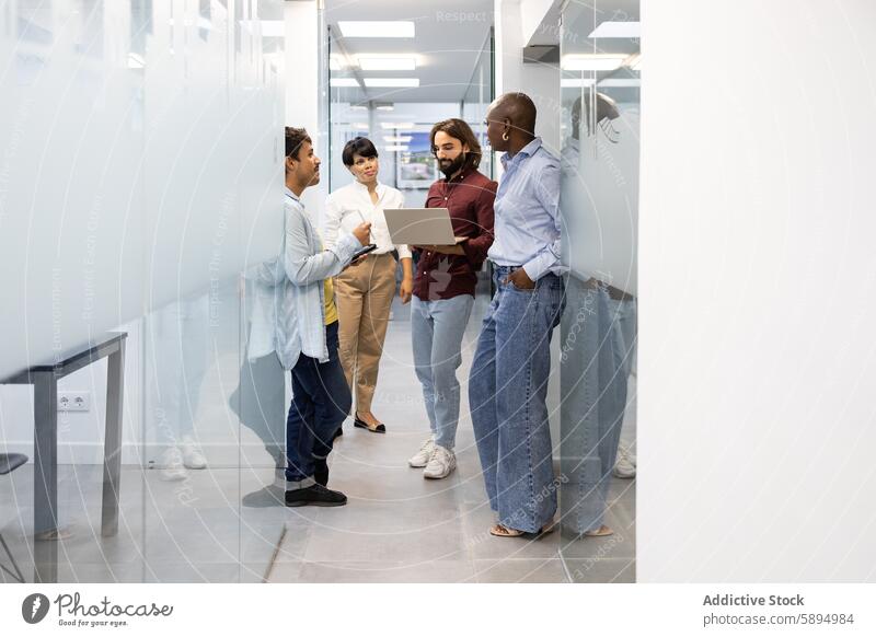 Diverse team discussing project in modern hallway office professional multicultural discussion corridor digital collaboration group diverse laptop standing