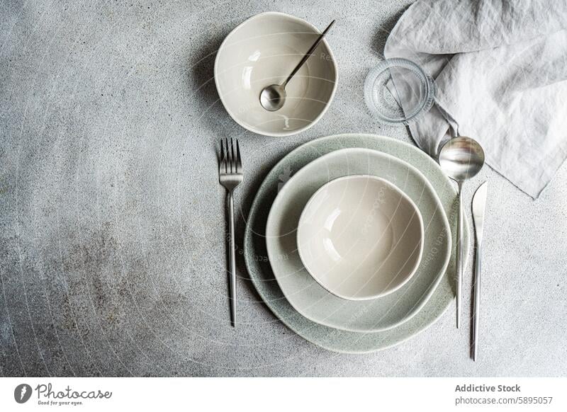 Elegant minimalist table setting with neutral tones minimalistic elegant plate stack muted small bowl silver cutlery fork spoon knife linen napkin textured grey