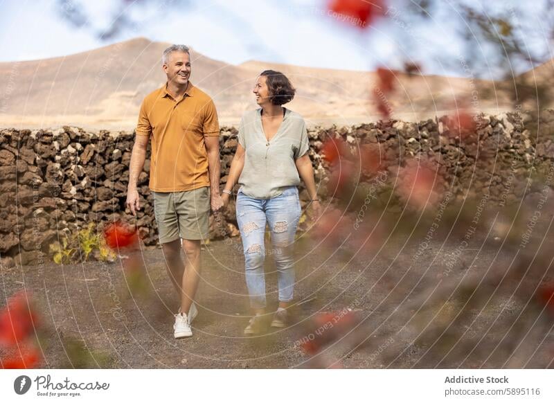 Couple walking together in a scenic landscape couple man woman summer casual joyful rustic stone wall volcanic happy holding hands flowers vibrant middle-aged