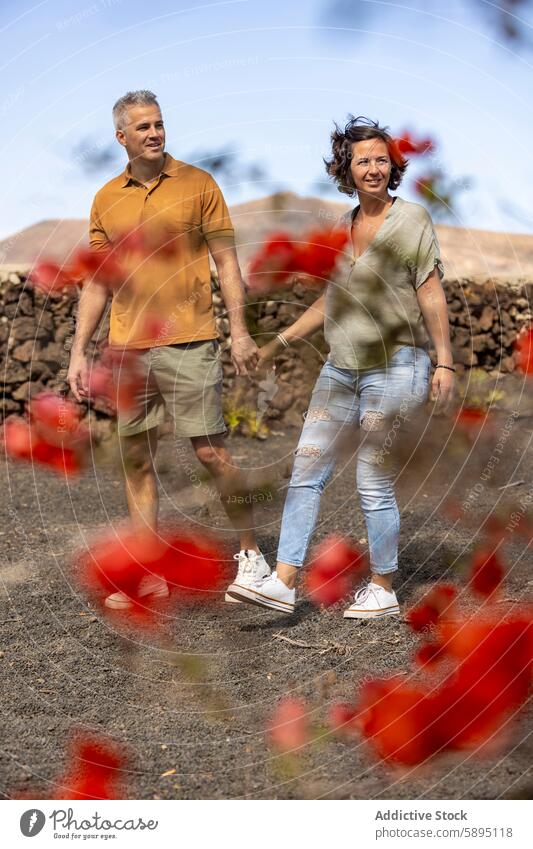 Casual walk through flower garden, couple holding hands man woman red flowers blurred foreground nature path casual relaxation partnership leisure outdoor plant