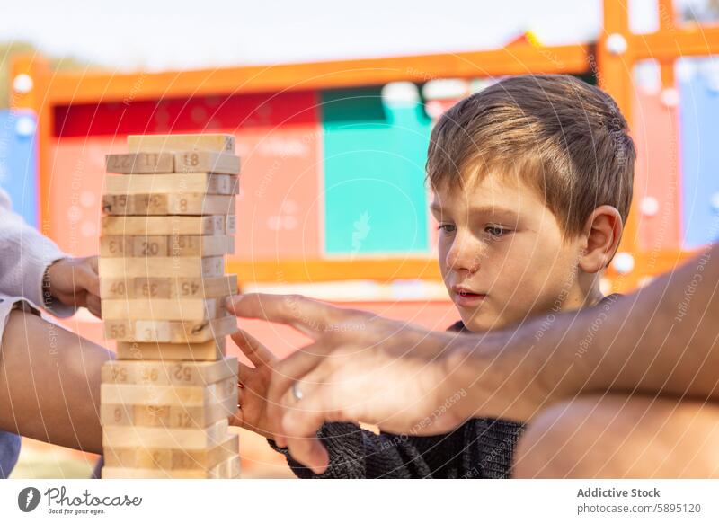 Boy playing game at playground with family boy block stack jenga strategy mother son concentration autumn outdoor leisure focus connection interaction child kid