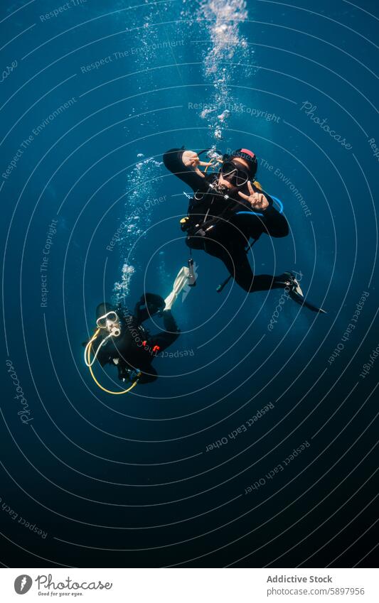 Divers in peaceful underwater scene in vivid blue ocean diver male female bubbles gesture peace sign clear water wetsuit mask snorkel fins expedition