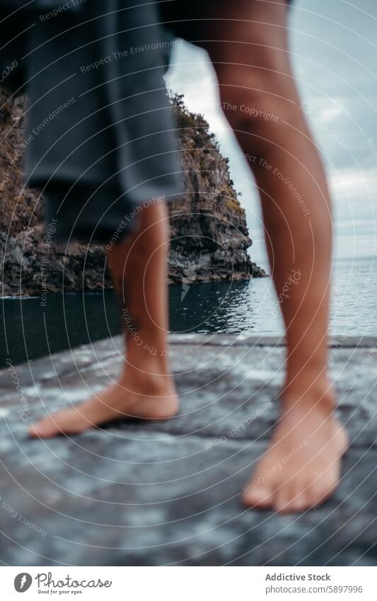 Barefoot young person on a coastal cliff in Sao Miguel, Azores. azores sao miguel nature outdoor barefoot rocky ocean sea coastline rugged serene connection