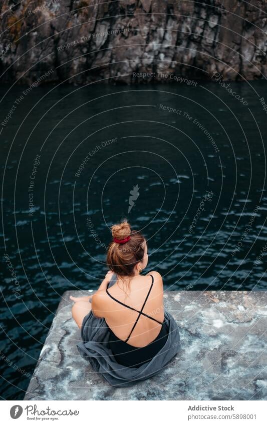 Young woman in contemplation by a rocky cove in Sao Miguel. cliff water solitude serene rugged platform sao miguel azores tranquil nature outdoor peaceful