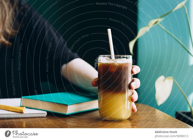 Student enjoys cold beverage while studying student coffee book notebook pen table drink education learning caffeine refreshment chilled glass straw hand