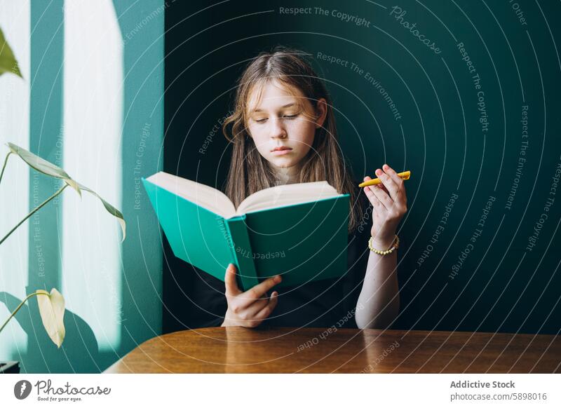 Young girl concentrating on a green book at table reading concentration education study learning seated young student back to school academic literacy focus