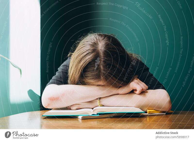 Female student resting head on arms with open book on desk school female education studying tired stress classroom learning exhausted fatigue teenager