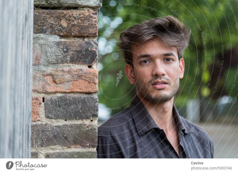 Young man from India leans against a wall and looks into the camera Man Athletic sexy portrait Muscular kind Congenial Looking into the camera full of relish