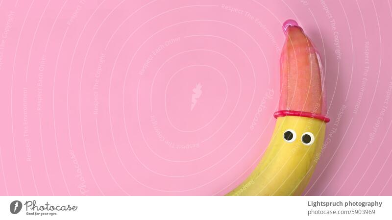 Banana with googly eyes and red condom hat on pink background. Safe sex concept. banana anthropomorphic humor sex education making a face sexual issues