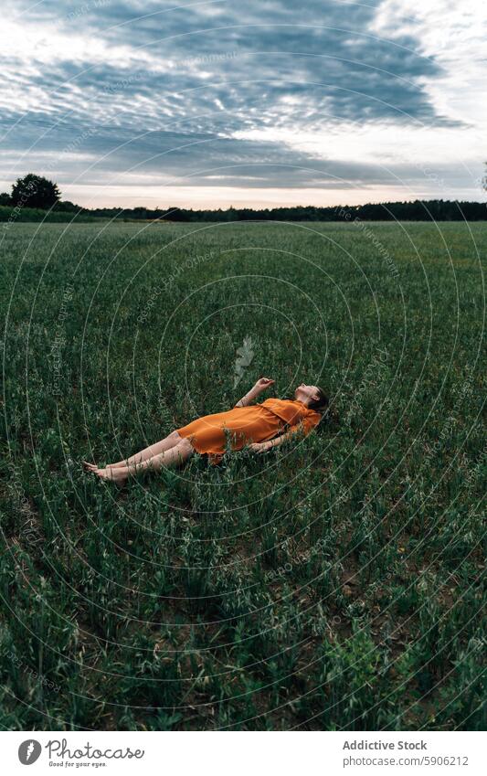 Woman relaxing in a field dressed in orange gown woman brunette eyes closed orange dress nature relaxation serene peaceful tranquility green grass harmony