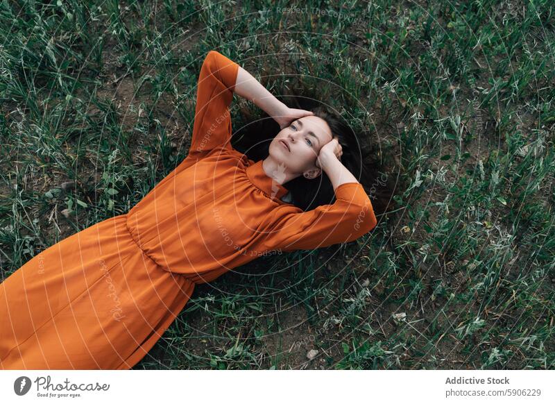 Young brunette woman relaxing in a field with eyes closed relaxation nature grass dress orange serenity peaceful rest young looking away lying down calm