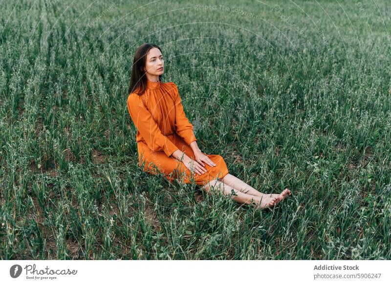 Woman relaxing in a green field dressed in orange woman orange dress brunette thoughtful contemplative nature outdoors serene tranquil calm peaceful relaxation