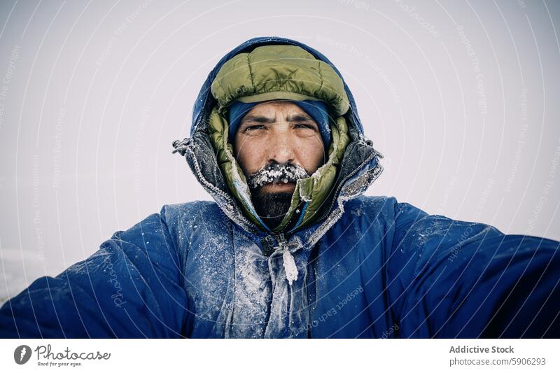 Male mountaineer in frozen gear braves harsh winter male extreme cold kyrgyzstan frost beard hood gaze looking at camera outdoor adventure survival selfie