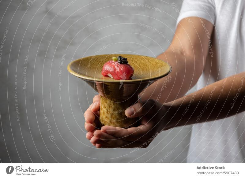 Man holding a sushi dish with careful precision chef hand ceramic caviar gourmet cuisine japanese food presentation culinary art seafood rice fish raw texture