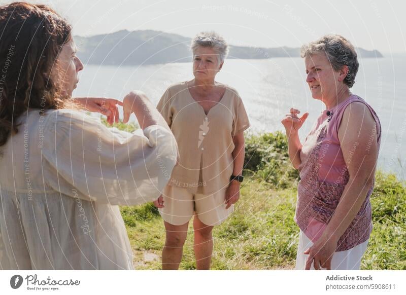 Senior friends communicating with sign language by the sea senior elderly mature communication seaside cliff outdoor friendship caucasian gesture conversation